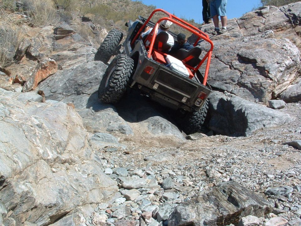 Off-road vehicle with red roll cage climbing rocky terrain