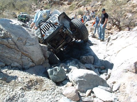 1981 Ford F-150 - A group of people watch as a white Jeep Wrangler navigates a difficult rocky obstacle.