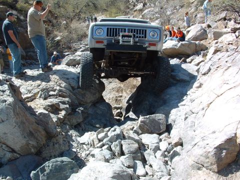 1981 Ford F-150 - An off-road vehicle carefully maneuvers over large rocks on a steep, dry creek bed.