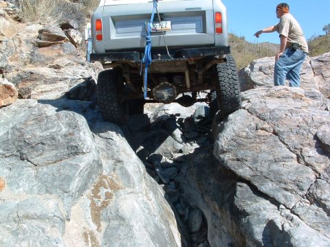 1981 Ford F-150 - A man points towards a gray SUV as it carefully maneuvers over large rocks on a desert trail.