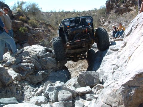 1981 Ford F-150 - A modified Jeep navigates a difficult rocky terrain with spectators observing the action.