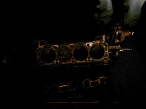 1986 Ford Bronco - An engine block with four cylinders is shown, with a person's legs visible in the background.