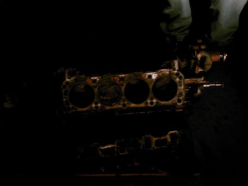 Engine block with four cylinders visible, dark and oily, with a person's legs in jeans above