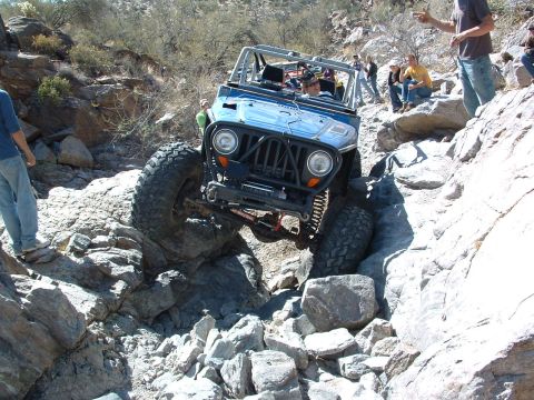 1981 Ford F-150 - A blue off-road jeep navigates a challenging rocky trail with spectators watching.