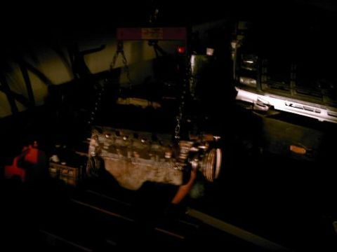 1986 Ford Bronco - Engine being removed or installed with a hoist, with a vehicle partially visible in the dark.