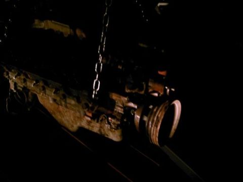 1986 Ford Bronco - A close-up view of a rusty engine component suspended by chains in a dark environment.