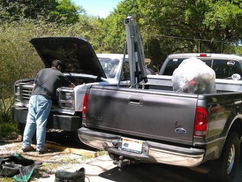 1986 Ford Bronco - Man works on the engine of a white Ford truck, with another Ford truck beside it.