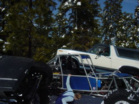 1986 Ford Bronco - A white 1986 Ford Bronco with a blue stripe is parked in a snowy wooded area next to a dune buggy.