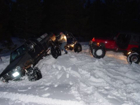 1986 Ford Bronco - Multiple off-road vehicles are stuck in the snow during nighttime conditions.