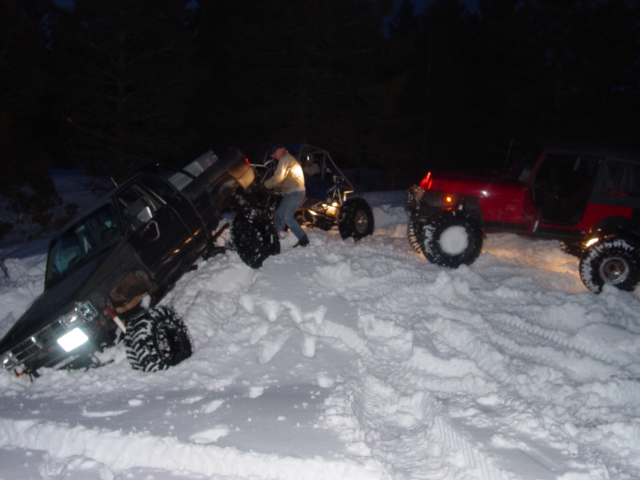 Black truck and red Jeep stuck in deep snow at night, with a person near the truck
