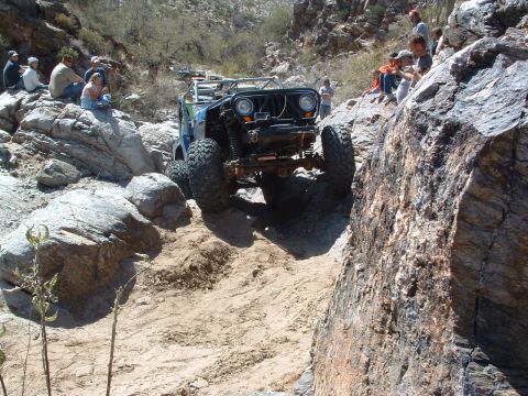 1981 Ford F-150 - An off-road vehicle tackles a challenging rocky terrain, with onlookers observing the difficult climb.