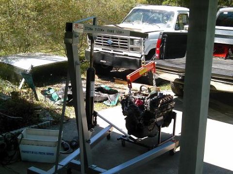 1986 Ford Bronco - An engine hoist is positioned to lift a V8 engine, with a Ford truck nearby.