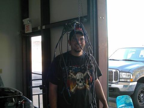 1986 Ford Bronco - A man stands in a garage doorway with spark plug wires draped around his head, while a gray truck is visible in the background.