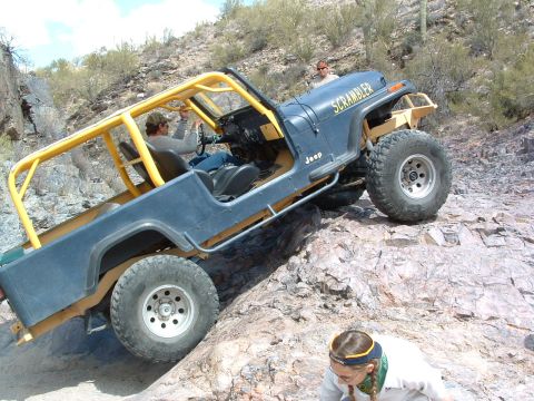 1981 Ford F-150 - A Jeep CJ-8 Scrambler navigates a rocky trail with a driver and passenger inside.