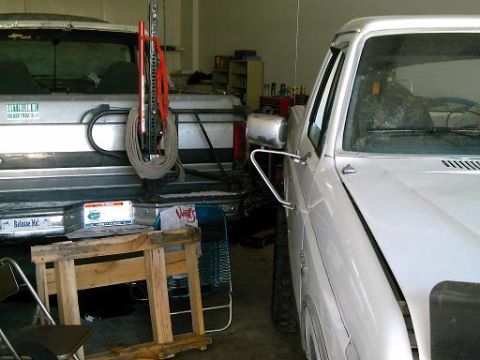 1986 Ford Bronco - Two pickup trucks are parked side-by-side in a garage, with a Hi-Lift jack visible on the rear of the silver truck.