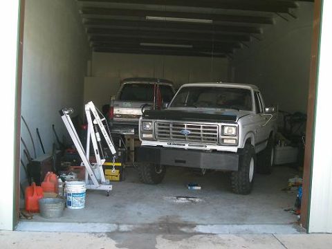 1986 Ford Bronco - A silver Ford truck with a black hood sits in a garage next to another vehicle.