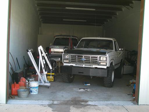 Silver Ford truck with black hood and aftermarket bumper in a garage