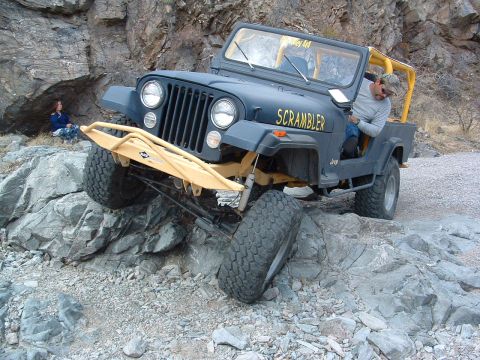 1981 Ford F-150 - This modified Jeep CJ-8 Scrambler is tackling a challenging rocky trail with a driver behind the wheel.