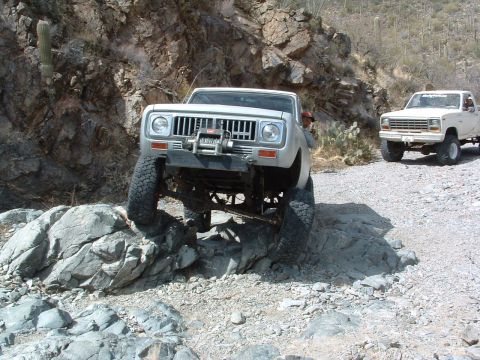 1981 Ford F-150 - Two off-road trucks navigate a rocky, desert terrain.