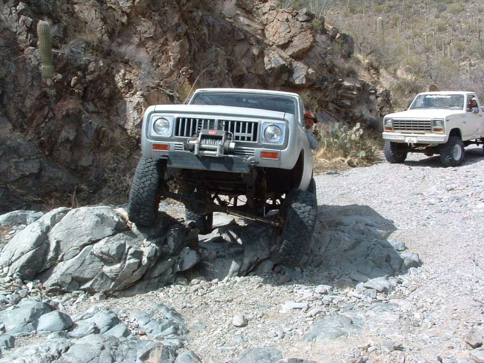 Silver off-road truck with a winch on the front, climbing over rocks