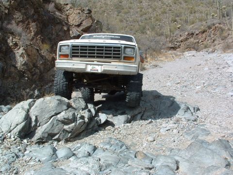 1981 Ford F-150 - Ford F-Series truck with lifted suspension and off-road tires driving over rocks in a desert landscape.