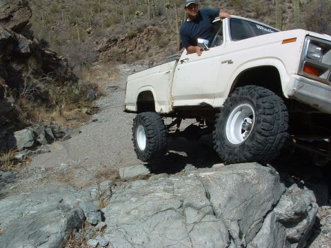 1981 Ford F-150 - A man drives a lifted pickup truck over rocky terrain in a desert landscape.