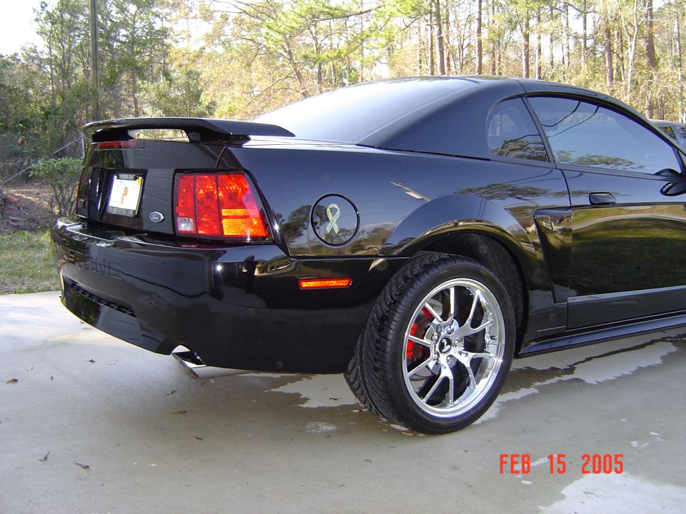 Rear three-quarter view of black Ford Mustang coupe with chrome wheels and spoiler on a driveway
