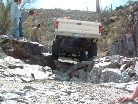 1981 Ford F-150 - A lifted pickup truck navigates a challenging rocky trail with spectators observing.