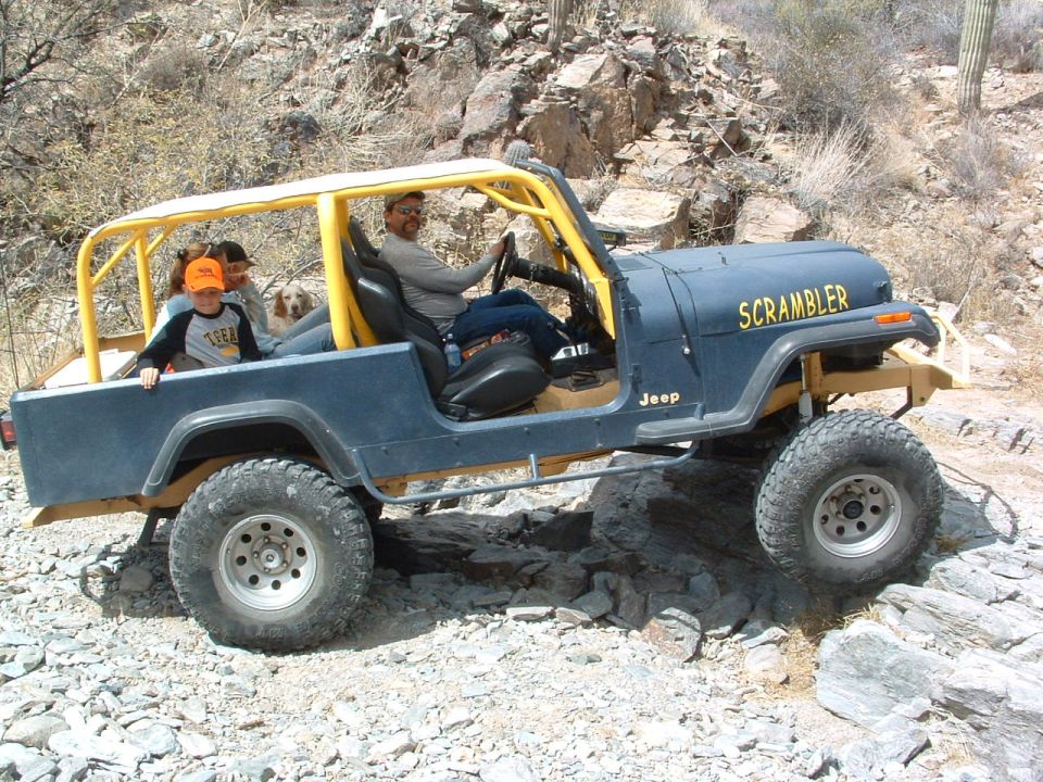 Blue Jeep Scrambler with yellow roll cage, side view, off-roading on rocks