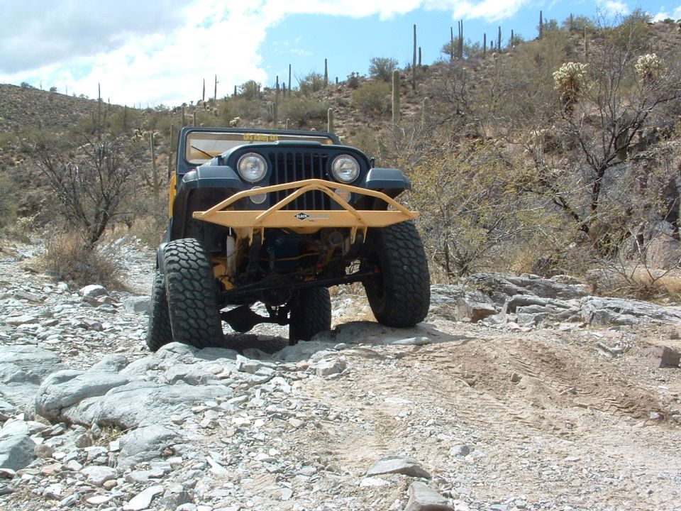 Jeep CJ-7 with yellow bull bar driving on rocky desert trail