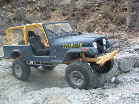 1981 Ford F-150 - A dark blue Jeep CJ-8 Scrambler navigates a rocky trail with its yellow roll cage and bumper visible.