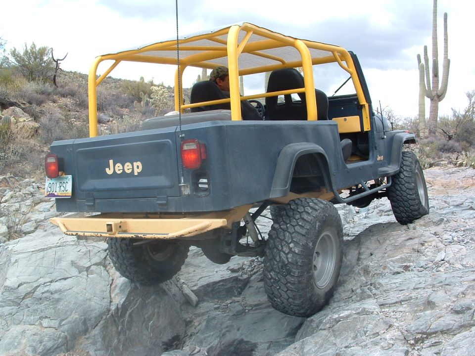 Dark blue Jeep CJ-7 with yellow roll cage on rocky terrain