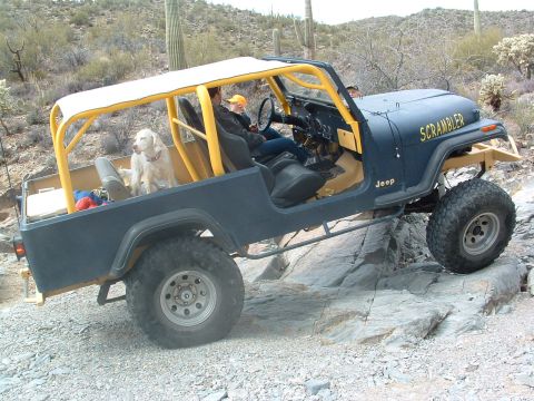 1981 Ford F-150 - Jeep CJ-8 Scrambler navigating rocky terrain with a dog in the passenger seat.