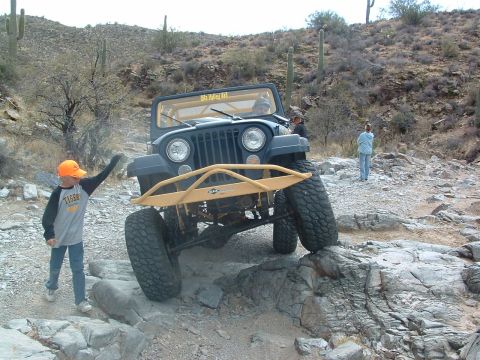 1981 Ford F-150 - A Jeep CJ-7 tackles a challenging off-road course with a young spectator watching.