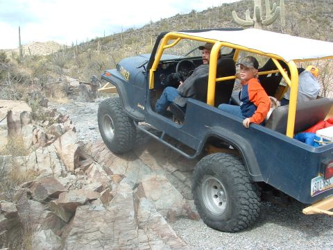 1981 Ford F-150 - A blue Jeep CJ-7, modified for off-roading, tackles a rocky trail with two occupants.