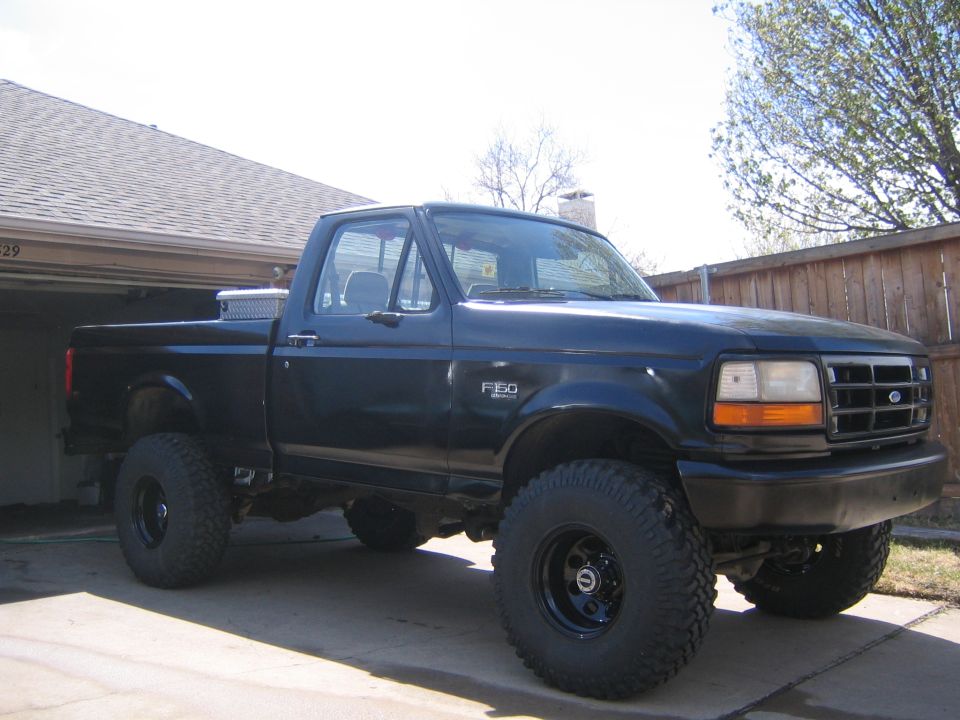 Black Ford F-150 pickup truck with lifted suspension and large tires parked in a driveway