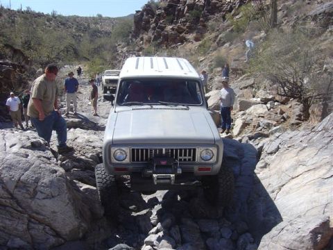 1981 Ford F-150 - An International Scout II is driven over a challenging rocky terrain, with other vehicles and onlookers present.
