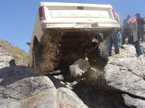 1981 Ford F-150 - A white Ford truck navigates a rocky terrain, kicking up dirt as it goes.