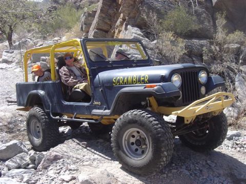 1981 Ford F-150 - A Jeep CJ-8 Scrambler navigates a rocky trail, its distinctive "Scrambler" decal visible on the side.