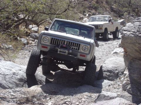 1981 Ford F-150 - Two off-road vehicles are shown traversing a rocky trail in a desert-like environment.