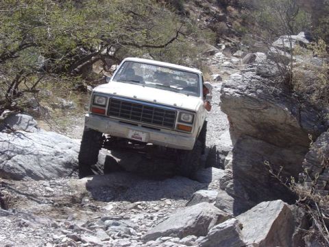 1981 Ford F-150 - A white Ford pickup truck is shown traversing a difficult, rocky terrain.