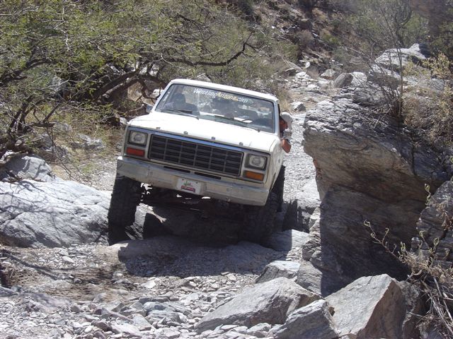 White Ford pickup truck navigating a rocky, off-road trail