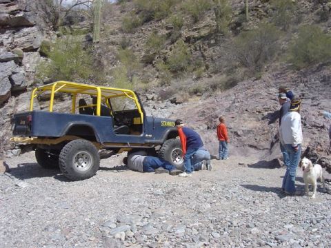 1981 Ford F-150 - A group of people are gathered around a blue Jeep Wrangler with a yellow roll cage, some working on its underside.