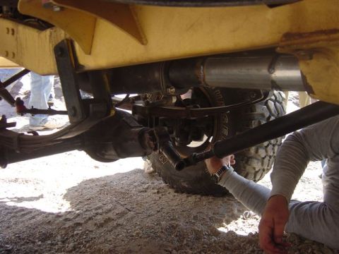 1981 Ford F-150 - A person works on the rear suspension and driveshaft of a yellow vehicle, focusing on the undercarriage components.