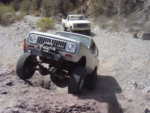 1981 Ford F-150 - Two off-road vehicles navigate a challenging rocky path in a desert-like environment.