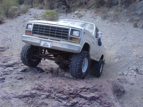 1981 Ford F-150 - A heavily modified pickup truck navigates a rocky, off-road trail. The vehicle appears to be from the early 1980s.