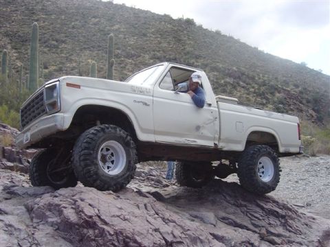 1981 Ford F-150 - A man drives a modified white Ford F-150 pickup truck off-road through a desert landscape.