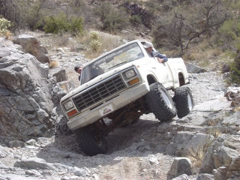 1981 Ford F-150 - A white pickup truck is shown off-roading on a rocky, mountainous terrain.