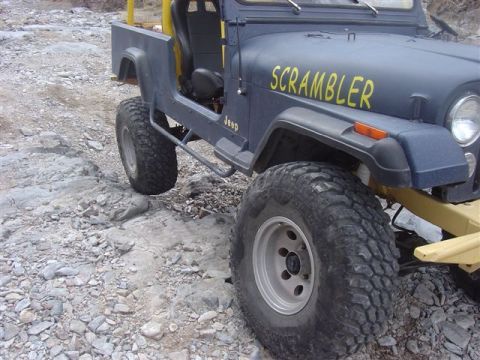 1981 Ford F-150 - A dark blue Jeep CJ-8 Scrambler with prominent "SCRAMBLER" lettering is parked on a rocky surface.