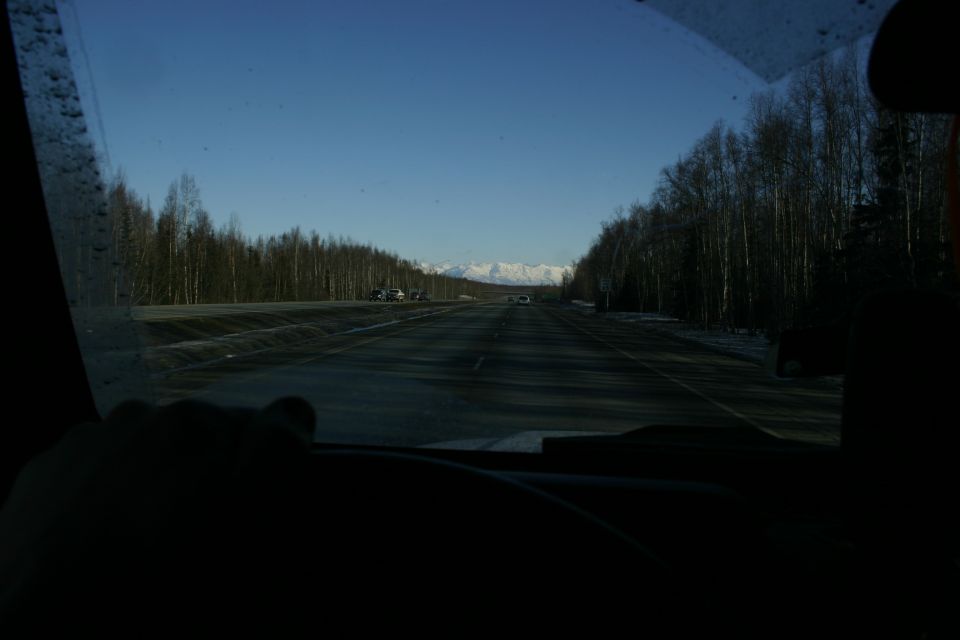 View from inside a vehicle looking out at a highway with trees and distant mountains under a clear blue sky